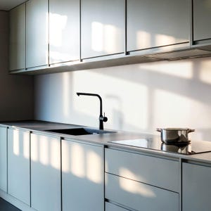 May include: A modern kitchen with white cabinets, a black faucet, and a stainless steel stovetop. The countertop is made of a light-colored material, and there is a pot on the stovetop.