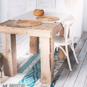Könnte beinhalten: Ein Holztisch mit einer weißen Tischdecke und zwei geflochtenen Platzsets. Ein weißer Stuhl steht am Tisch. Der Tisch steht auf einem gemusterten Teppich in den Farben Türkis, Grau und Weiß.