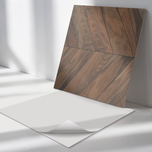 May include: A close-up of a brown wood-look tile with a chevron pattern. The tile is sitting on a white surface.