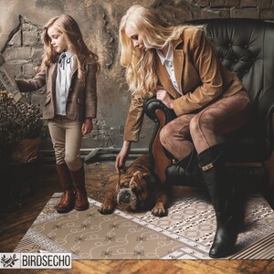 May include: A brown and white patterned rug with a brown and white bulldog lying on it. A woman in a brown jacket and brown trousers is sitting in a black leather chair. A young girl in a brown jacket and white shirt is standing next to the rug, holding a newspaper.