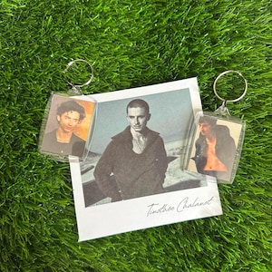 May include: Two rectangular clear acrylic keychains featuring portraits of Timothée Chalamet, alongside a square photographic print of the actor wearing a dark sweater with the handwritten name Timothée Chalamet in the bottom right corner.