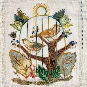 May include: Embroidered artwork featuring two birds in a cage with a sun and leaves. The birds are brown and white with black spots. The leaves are green, brown, and yellow. The sun is yellow with a brown circle in the center.