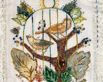 May include: Embroidered artwork featuring two birds in a cage with a sun and leaves. The birds are brown and white with black spots. The leaves are green, brown, and yellow. The sun is yellow with a brown circle in the center.