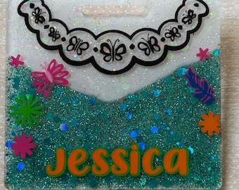 May include: A teal glitter resin keychain with a white background. The keychain features a black butterfly design, a white glitter border, and the name "Jessica" in orange letters.