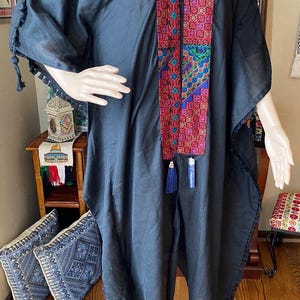 May include: A black kaftan with a long, colorful embroidered trim. The trim features geometric patterns in shades of red, blue, green, and pink. The kaftan has a loose, flowing fit and is made of a lightweight fabric.