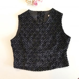 May include: A sleeveless black velvet top with a raised floral pattern. The top has a V-neck and a tailored fit. The fabric has a subtle sheen, and the design is visible across the entire garment. The top is likely for formal or semi-formal occasions.