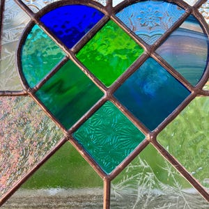 May include: A stained glass window with a heart-shaped design. The heart is made up of blue, green, and clear glass pieces. The glass is textured and has a vintage look.