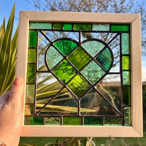 May include: A stained glass window panel featuring a green heart design. The heart is made up of smaller pieces of glass in various shades of green, creating a textured and intricate pattern.