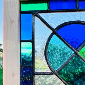 May include: A stained glass window with a geometric design featuring blue, green, and white glass pieces.