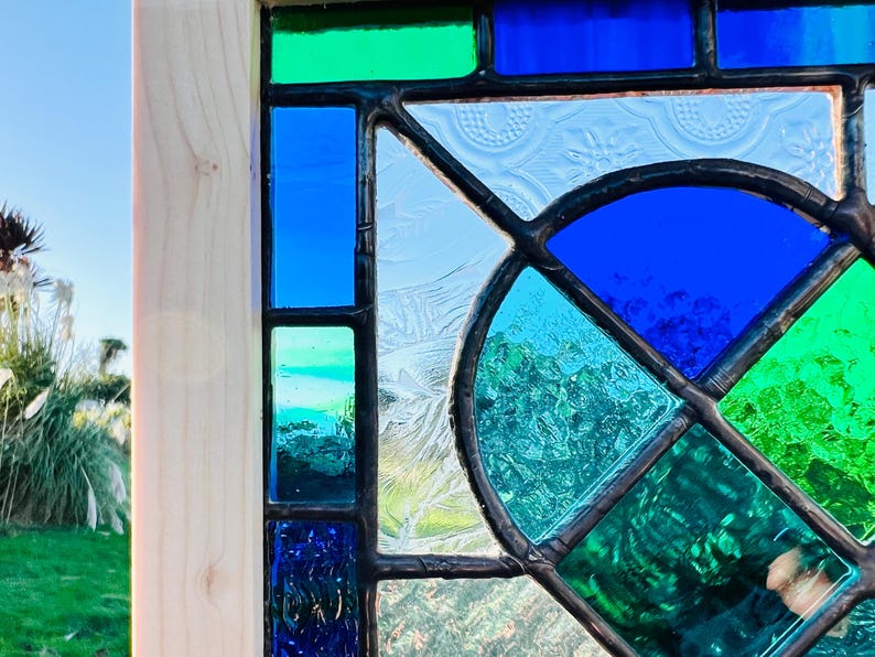 May include: A stained glass window with a geometric design featuring blue, green, and white glass pieces.