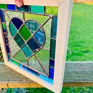 May include: A stained glass window panel with a heart shape design in shades of blue and green. The panel is framed in natural wood.