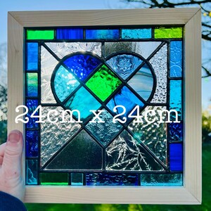 May include: A stained glass window panel featuring a heart design with blue, green, and white glass pieces. The panel is framed in wood and measures 24 inches by 24 inches.