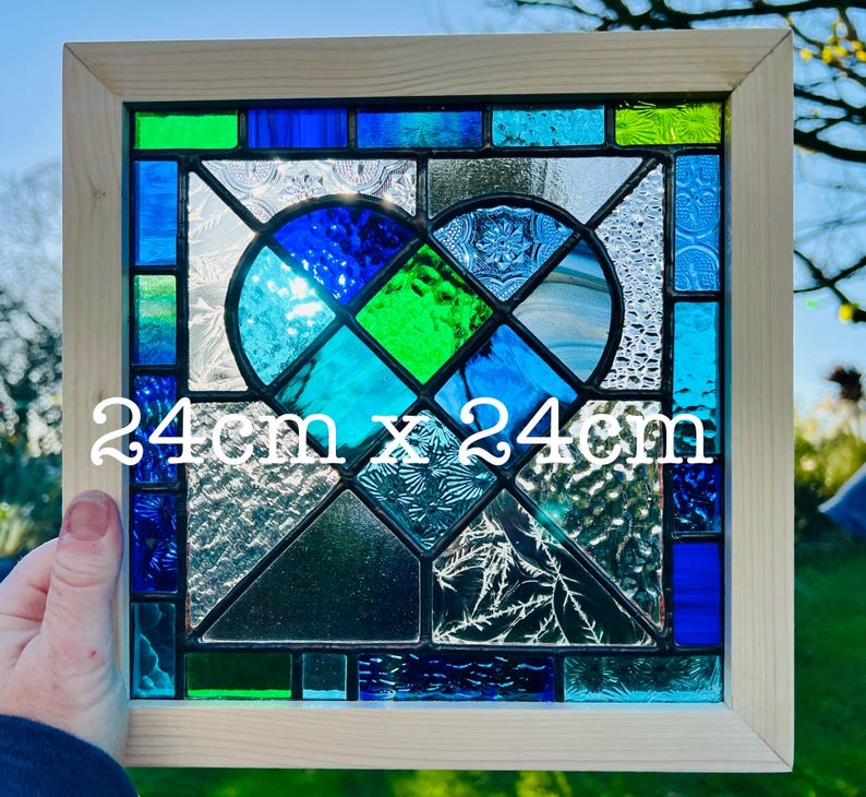 May include: A stained glass window panel featuring a heart design with blue, green, and white glass pieces. The panel is framed in wood and measures 24 inches by 24 inches.
