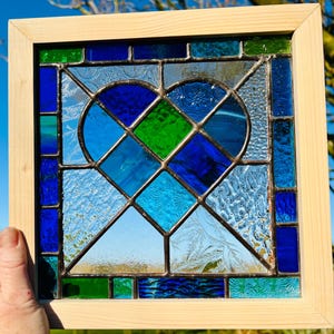 May include: A stained glass window panel featuring a blue and green heart design. The heart is made up of multiple pieces of glass, creating a geometric pattern. The panel is framed in wood.