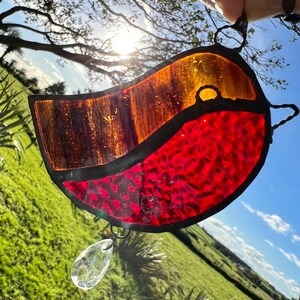 May include: A stained glass robin with red and orange glass, hanging from a window with a crystal prism hanging below.