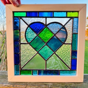 May include: A stained glass window featuring a heart design with blue, green, and clear glass pieces. The window is framed in natural wood.