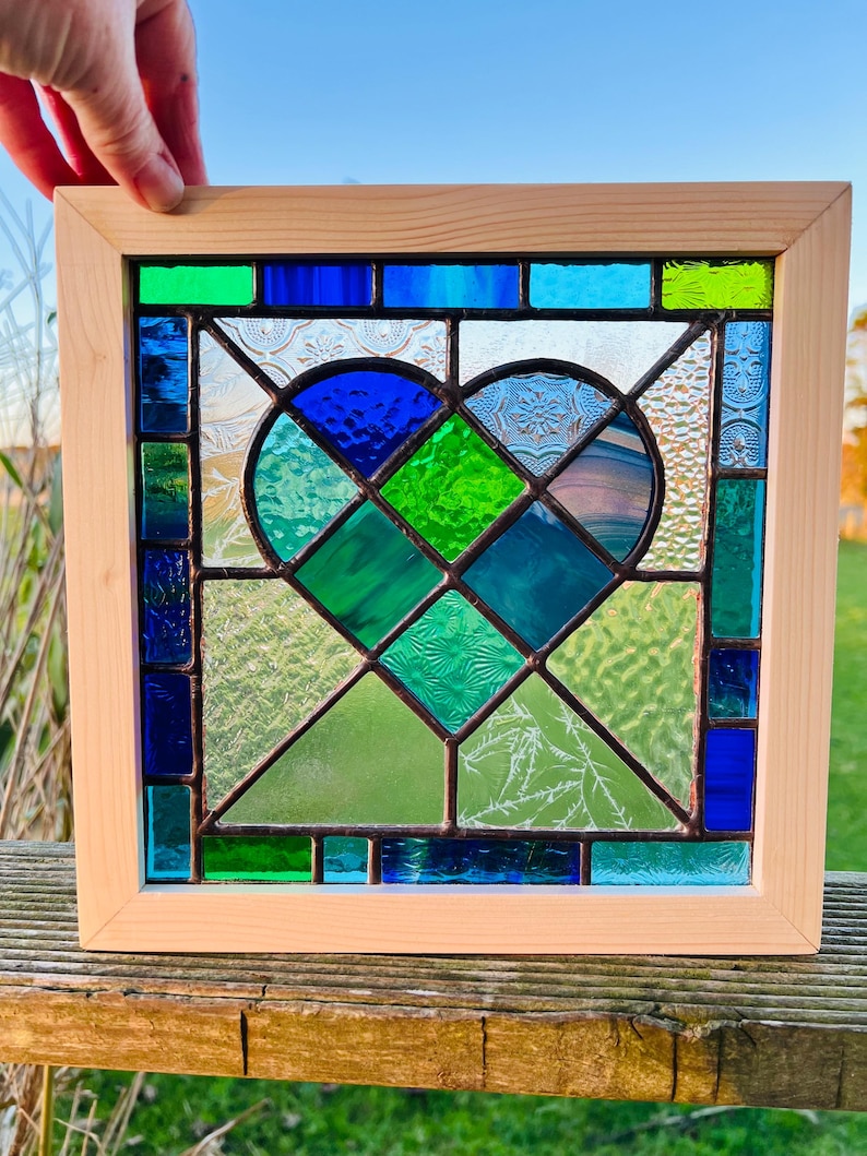May include: A stained glass window featuring a heart design with blue, green, and clear glass pieces. The window is framed in natural wood.