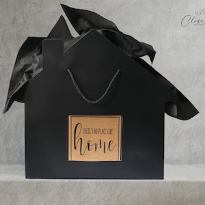 May include: Black house-shaped gift bag with a brown paper tag that says "There's no place like home".