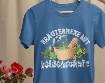 May include: A blue t-shirt with a white graphic of a mortar and pestle surrounded by flowers and the text "Kräuterhexe mit Heilkraft".