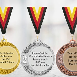 Könnte beinhalten: Drei Medaillen mit Bändern in den Farben der deutschen Flagge. Die goldene Medaille trägt den Text "Für die besten Großeltern der Welt Elisabeth & Anton." Die silberne Medaille trägt den Text "Ihr persönlicher Wunschtext mit einem Laser graviert. Ø50 mm Kunststoffemblem." Die bronzene Medaille trägt den Text "Team-Event Hotel**** Sonnenhof Mai 2024."