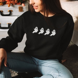 Op de afbeelding: Zwart sweatshirt met vier witte spookontwerpen over de borst. De geesten hebben eenvoudige, afgeronde vormen met kleine oog- en monddetails. Het sweatshirt is effen zwart van kleur en de geesten zorgen voor een contrasterend wit accent.