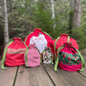 May include: Five red Christmas gift bags with green ribbon ties. The bags are decorated with different festive themes, including Santa Claus, plaid, and holly.