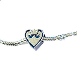 May include: A silver charm bracelet with a heart-shaped charm featuring a blue and white crown design.