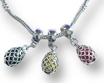 May include: A silver charm bracelet with three dangling charms. The charms are shaped like eggs and are decorated with green, yellow, and red rhinestones.