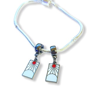May include: A silver charm bracelet with two charms featuring a white and red sun design. The charms are attached to the bracelet with silver beads.