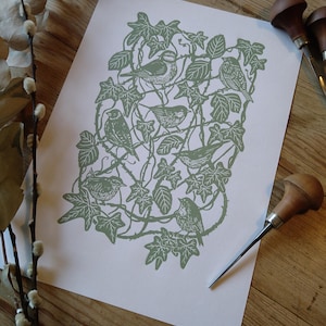 May include: A green print of birds in a leafy vine pattern. The print is on white paper and is surrounded by a wooden table.