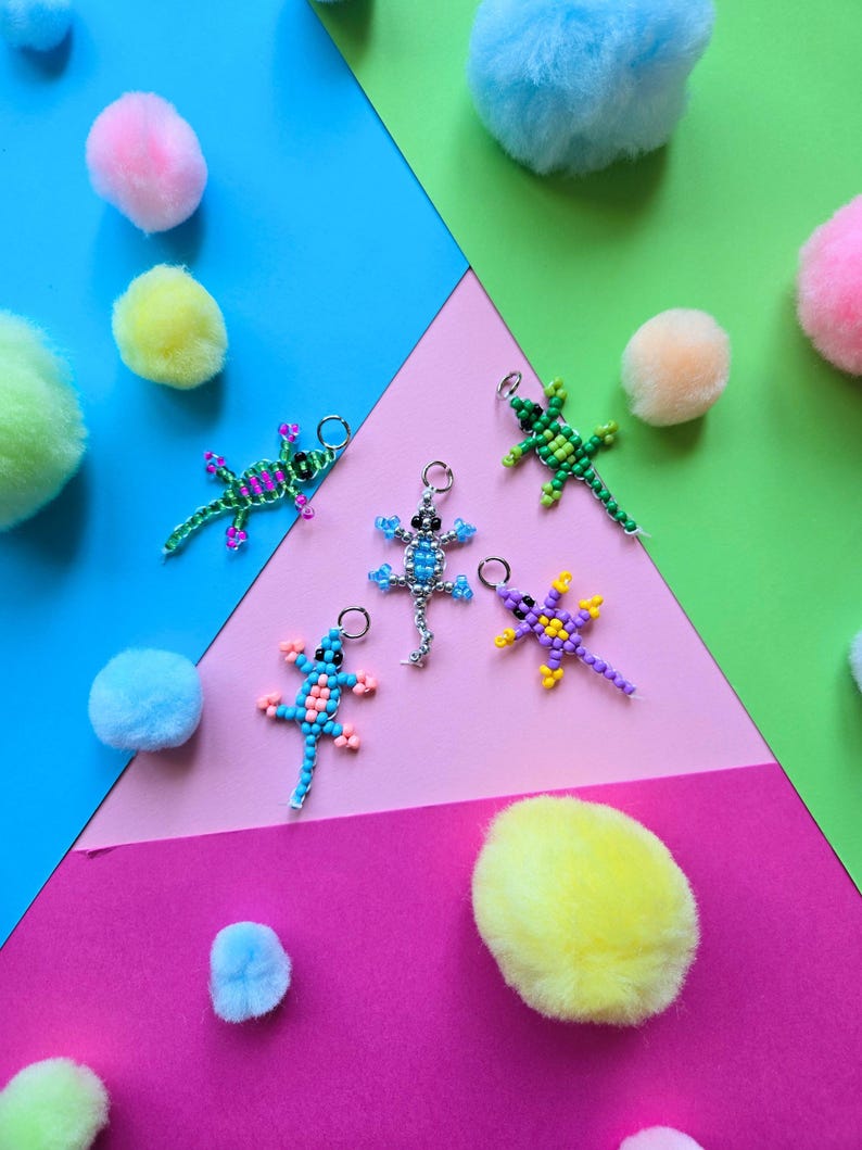 May include: Five lizard-shaped charms crafted from small colorful beads, each featuring a metal jump ring at the top. The lizards are designed in various color combinations including green and pink, light blue and pink, bright blue and white, green and yellow, and purple and yellow.
