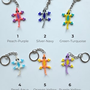 May include: Six lizard-shaped keychains made of small beads, each with a metal ring and chain. The designs are labeled 1 Peach-Purple, 2 Silver-Navy, 3 Green-Turquoise, 4 Pearl-Aqua, 5 Orange-Yellow, and 6 Purple-Yellow, showcasing various color combinations.