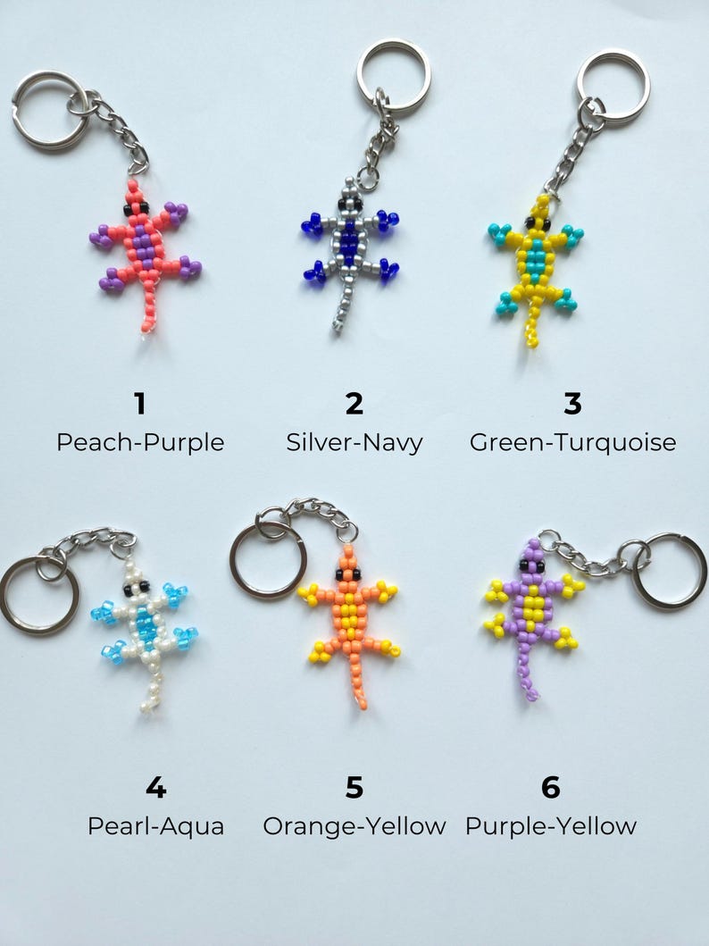 May include: Six lizard-shaped keychains made of small beads, each with a metal ring and chain. The designs are labeled 1 Peach-Purple, 2 Silver-Navy, 3 Green-Turquoise, 4 Pearl-Aqua, 5 Orange-Yellow, and 6 Purple-Yellow, showcasing various color combinations.