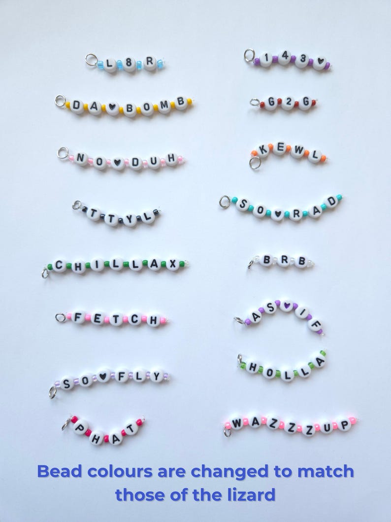 May include: A collection of small beaded charms featuring white alphabet beads with black letters and colorful accent beads. The charms display phrases like L8R, 143, DA BOMB, G2G, NO DUH, KEWL, TTYL, SO RAD, CHILLAX, BRB, FETCH, AS IF, SO FLY, HOLLA, PHAT, and WAZZZUP.