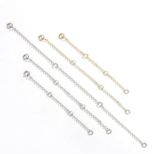 May include: Five silver and gold chain extenders with jump rings. The extenders are different lengths and are arranged in a row from shortest to longest.
