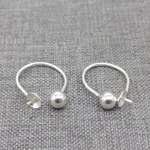 May include: Two silver earring findings with a round ball at the end. The findings are open and ready to be attached to earrings.