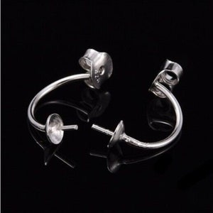 May include: Two silver earring findings with a curved wire and a small round cup at the end. The findings are designed to hold a pearl or other gemstone.