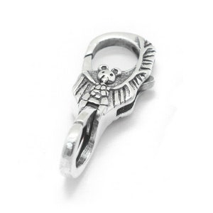 May include: Silver-toned metal clasp featuring an intricate design of a winged creature holding a small bear. The clasp has a spring-loaded mechanism for attaching to a chain or strap.
