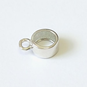 May include: A small, cylindrical silver-toned metal jewelry finding with a smooth, polished exterior surface and a circular loop attached to one side, designed for connecting components in jewelry making and craft projects.