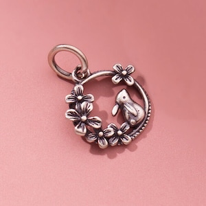 May include: Silver charm featuring a small rabbit inside a circle of flowers. The charm has a loop for attaching to a bracelet or necklace.