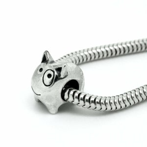 Könnte beinhalten: Ein silberner Anhänger in Form einer Cartoon-Katze mit einem großen Auge. Der Anhänger befindet sich an einer silbernen Schlangenkette.