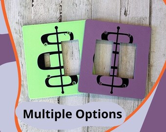 May include: Two light switch covers, one green and one purple, with a mid-century modern design. The design features a black abstract shape with rounded edges. "Multiple Options" is written in white text on a black background.