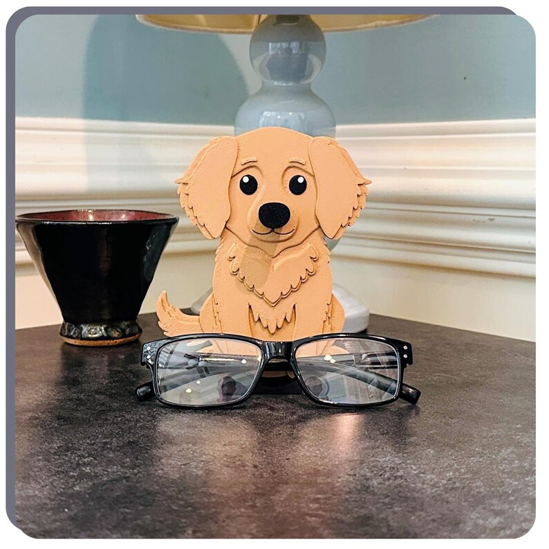 May include: A wooden golden retriever dog figurine holding a pair of black spectacles. The figurine is sitting on a dark surface.