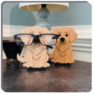 May include: Two wooden golden retriever dog figurines, one wearing black framed glasses, on a dark grey surface.