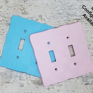 May include: Two light switch covers, one light blue and one pink, with a rough, textured surface. The text "Multiple Configurations Available" is written in black on a white background in the top right corner of the image.