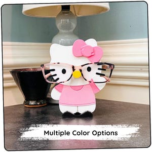 Peut inclure: Un personnage Hello Kitty rose avec des lunettes noires et un nœud rose. Le personnage est un support pour lunettes.
