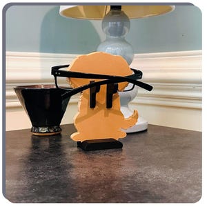 May include: A wooden figurine of a dog wearing glasses. The dog is brown and has a black base. The glasses are black and have a dark lens.