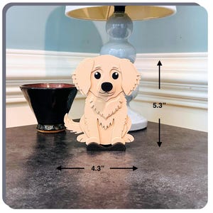 May include: A wooden figurine of a golden retriever dog, sitting with its paws together. The figurine is 5.3 inches tall and 4.3 inches wide.