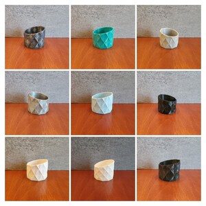 May include: Nine different colored geometric planters, each with a diamond pattern. The planters are made of a hard plastic material and are all the same size. The colors are black, gray, white, teal, and light blue.