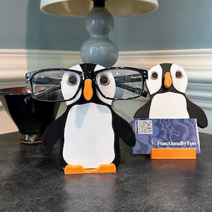 May include: Two black and white penguin figurines with orange beaks and feet. One penguin is wearing black framed glasses. The penguins are holding a business card that reads "Functionally Fun".